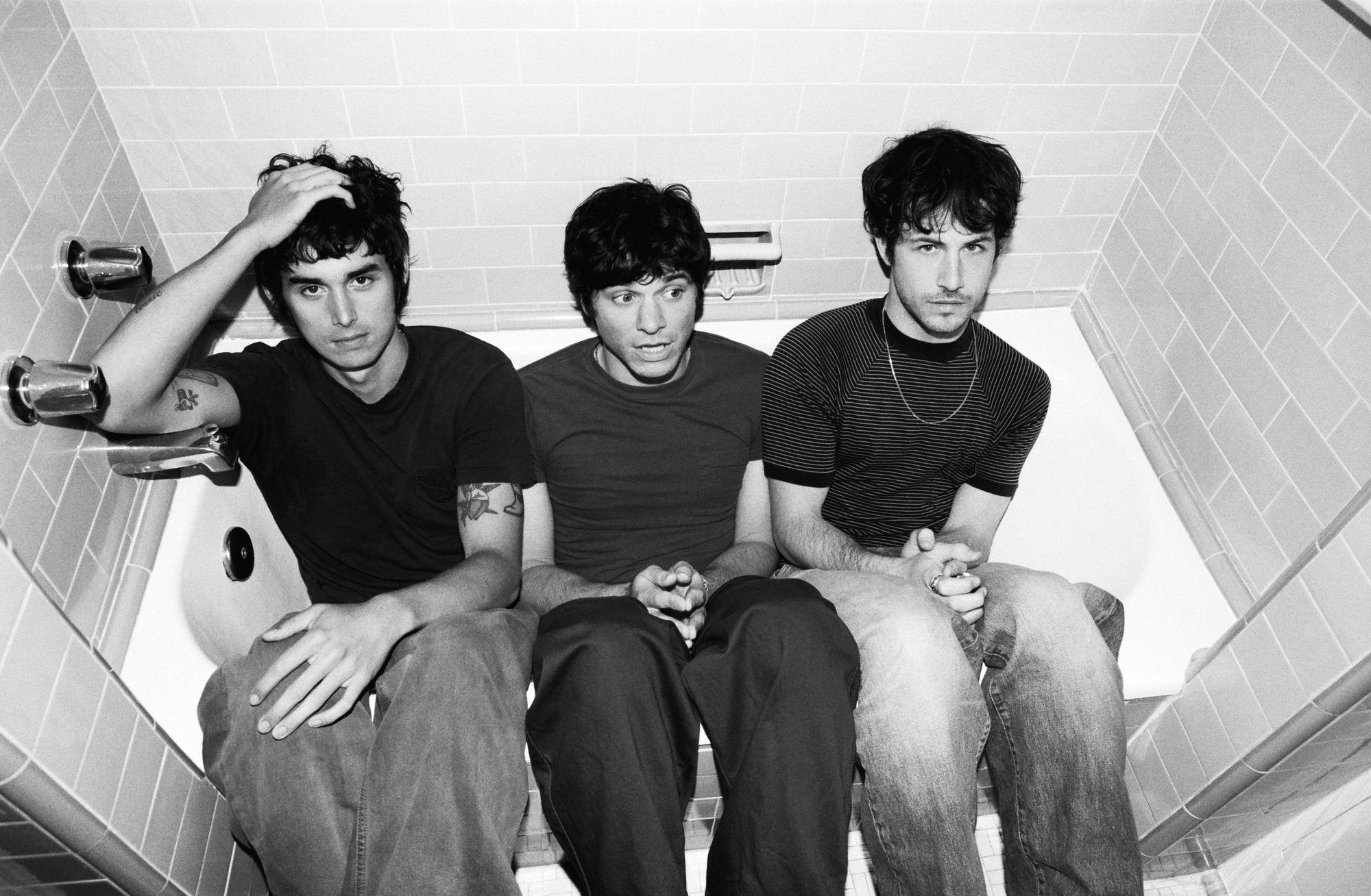 The three members of Wallows sitting in a bathtub while wearing T-shirts and jeans.