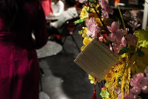 Photo of a bouquet with yellow and pink cloth flowers with a bamboo square and a red tassel hanging off of it.

