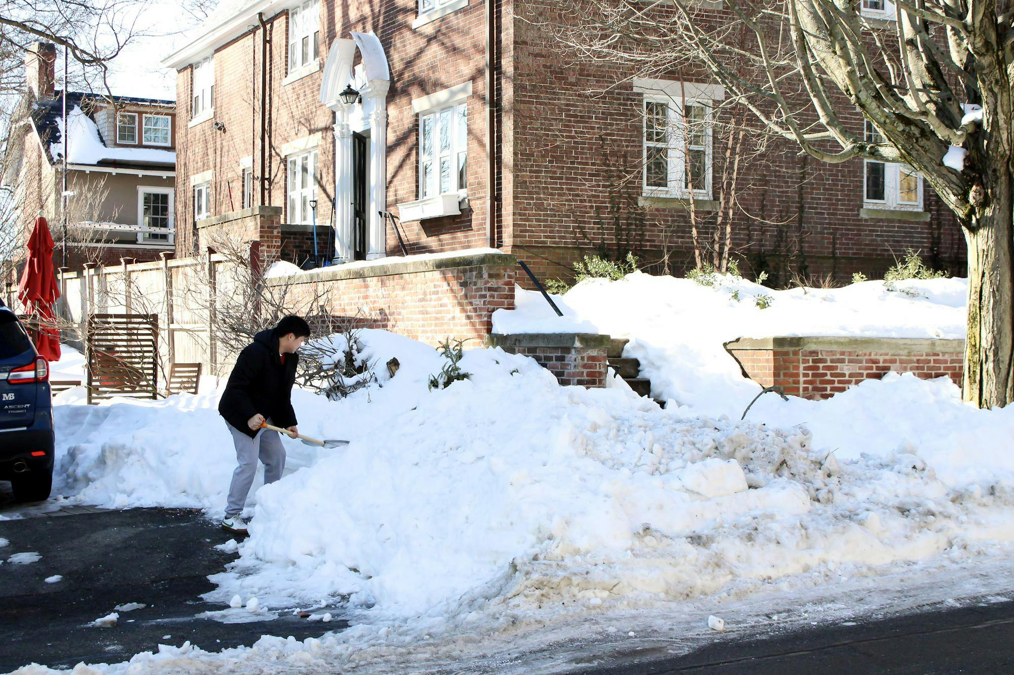 Photo of a person shoveling a pile of snow on a sidewalk.