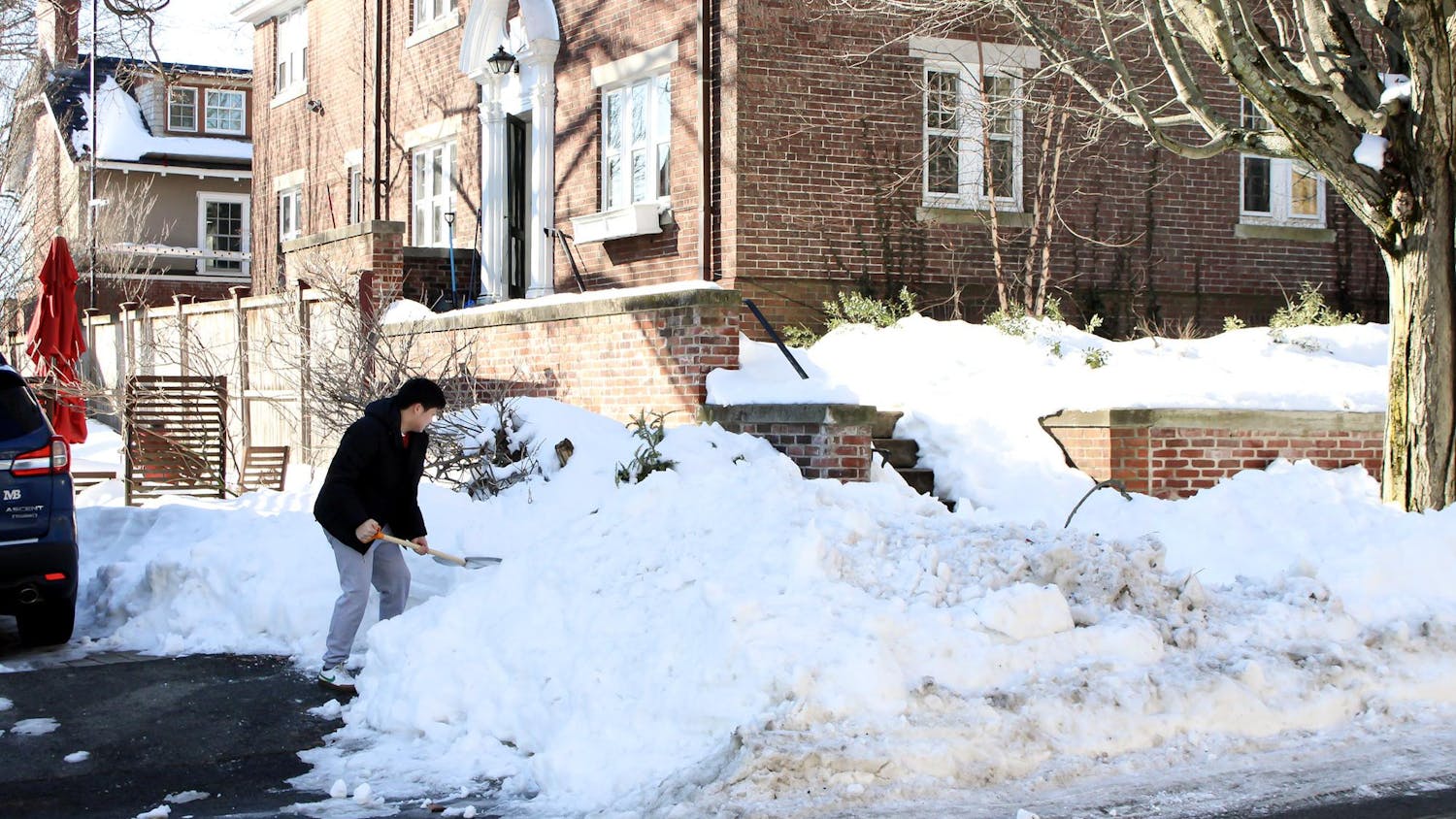 Photo of a person shoveling a pile of snow on a sidewalk.