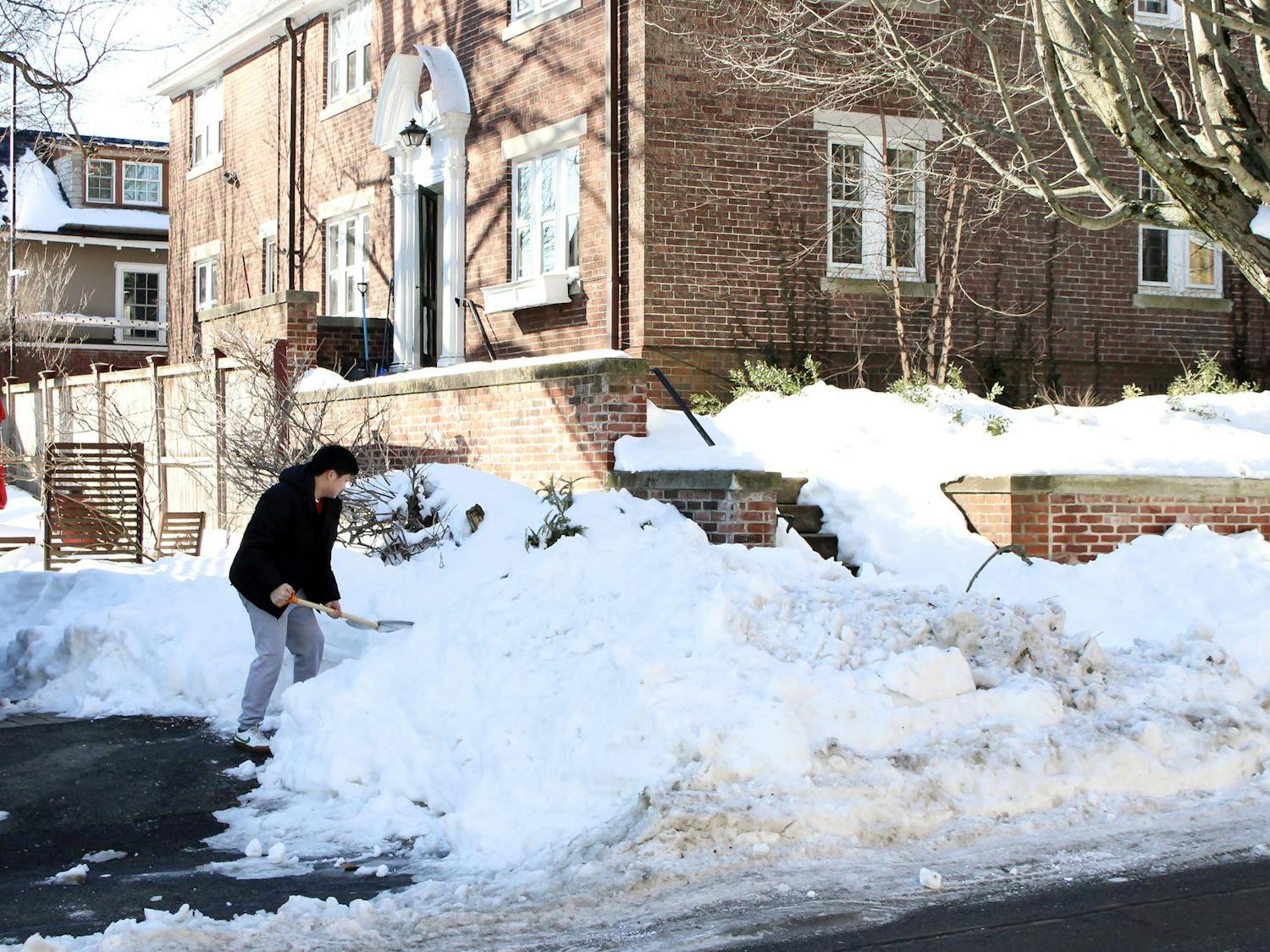 Photo of a person shoveling a pile of snow on a sidewalk.