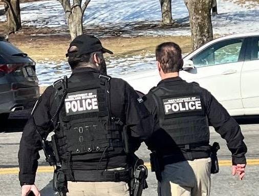The backs of two men in police vests. 