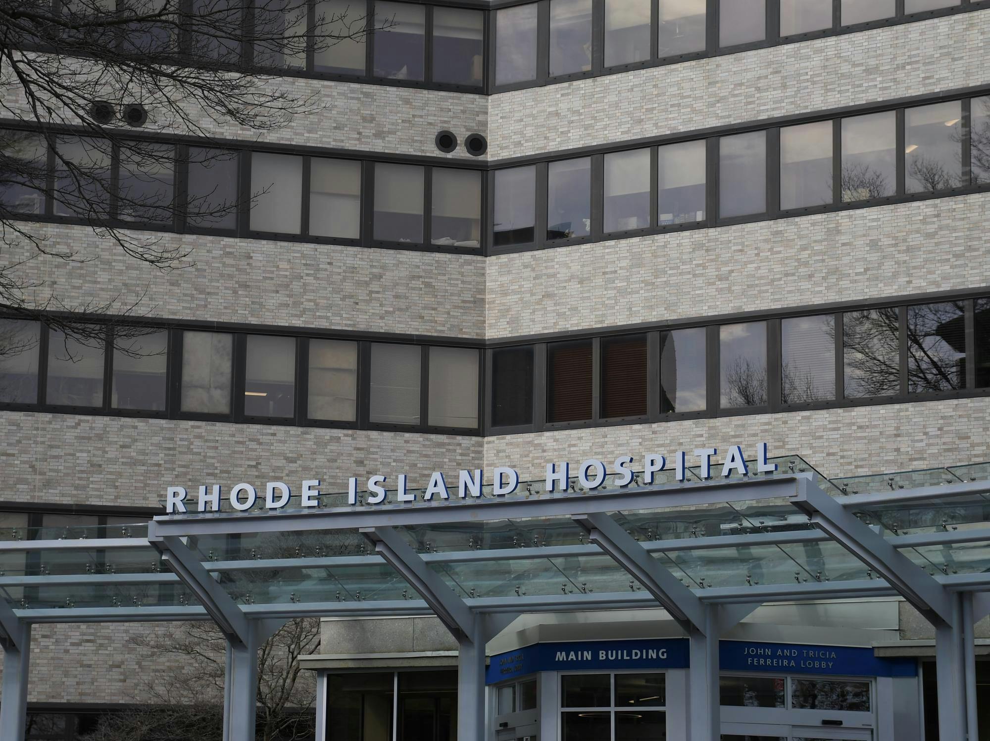 A sign that says "Rhode Island Hospital" on the front awning of a large tan brick building.