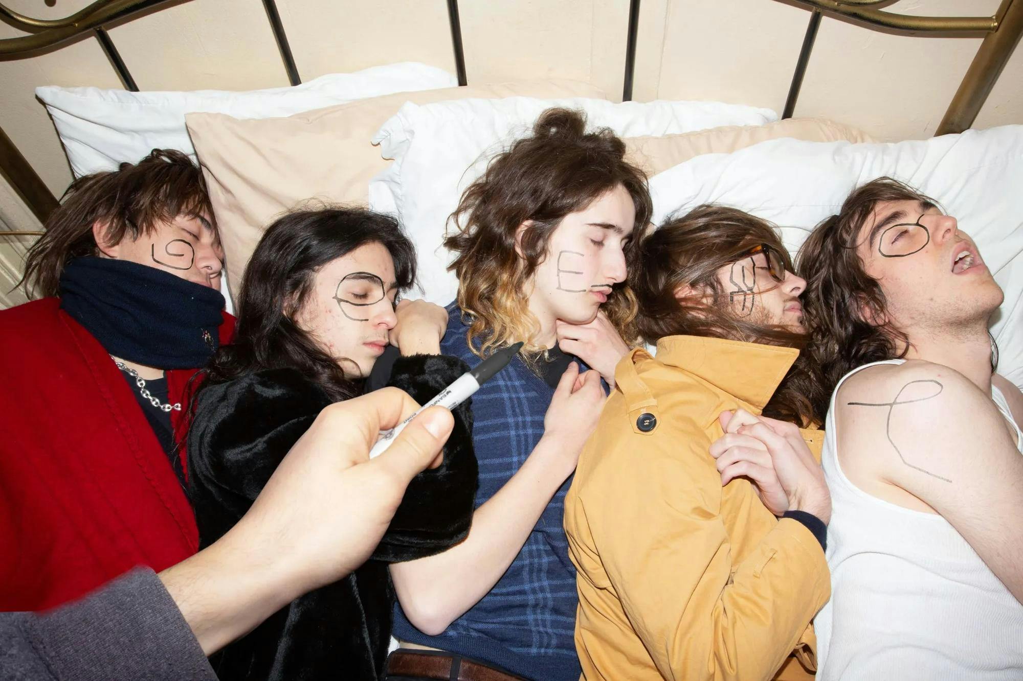 Photo of five individuals lying in bed next to each other with the letters G-E-E-S-E written on them respectively.