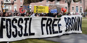 A large crowd of protesters on the Main Green hold a banner that says "Fossil Free Brown" and other signs in support of University divestment from fossil fuels.