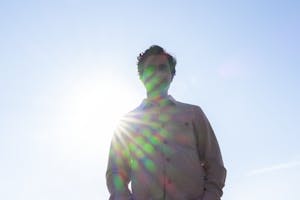 Karan Mahajan shot from below with clear blue sky in the background and sunshine rays radiating on his figure.