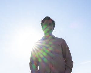 Karan Mahajan shot from below with clear blue sky in the background and sunshine rays radiating on his figure.