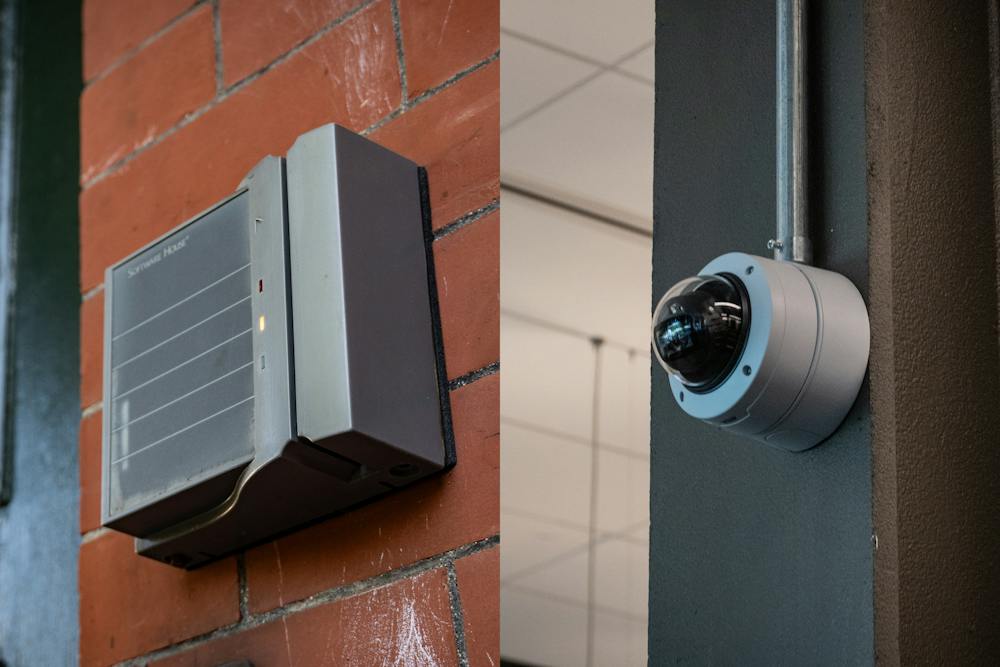 Left: A photo of a grey box with a thin slit on the right and three little red, yellow and green lights. Right: A photo of a round camera lens on a silver mount on a pole.

