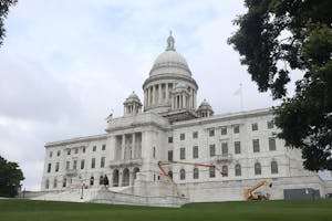 Image of the white Providence State House building. Branches in the foreground of the photo.