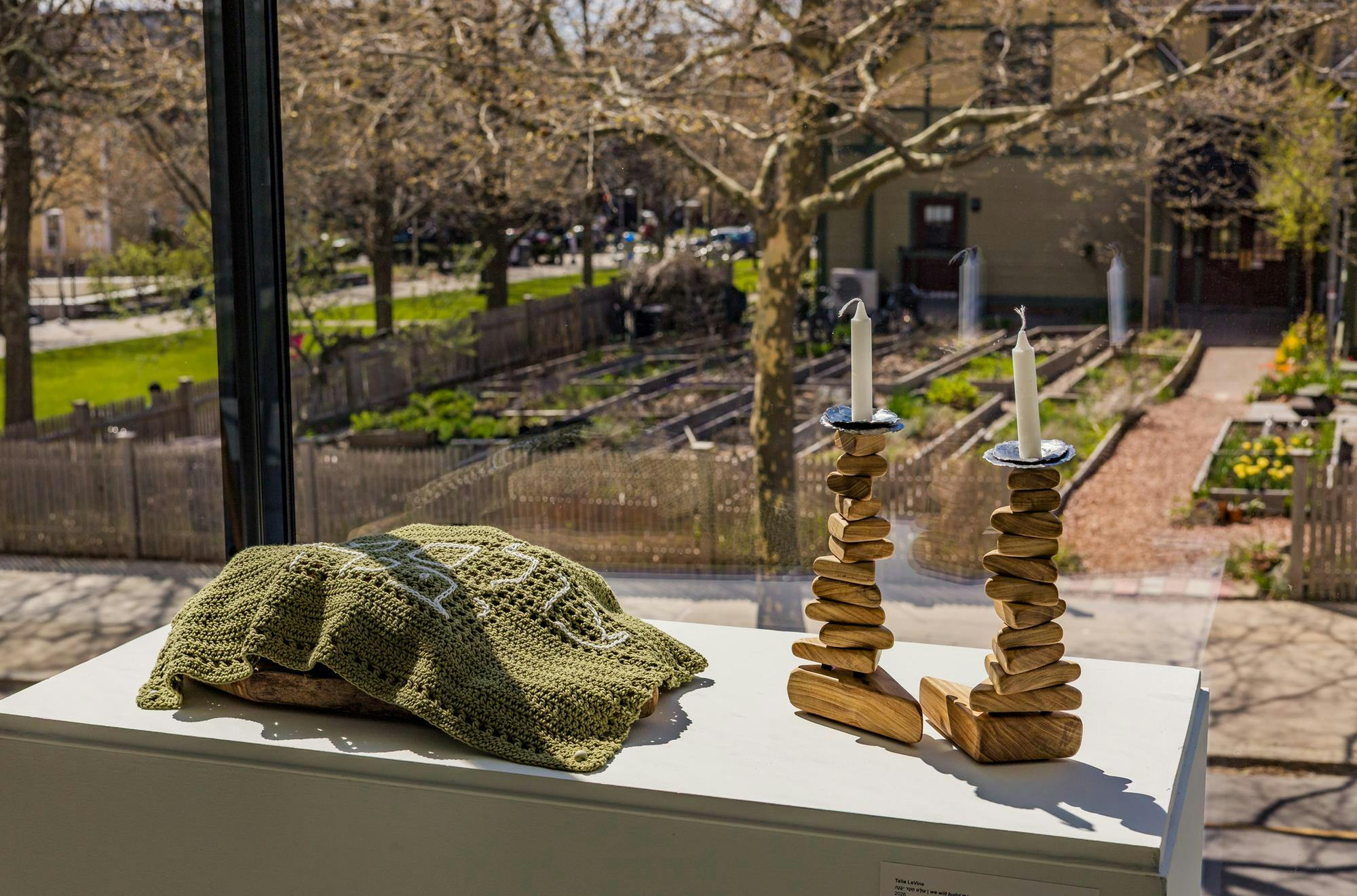 Photo of art pieces created by Talia LeVine ’27 displayed at the Brown Art Institute’s new “Point of Entry” exhibit. The piece on the left is a small green blanket covering a wooden bowl, and the piece on the right consists of two wooden towers with candles on top.