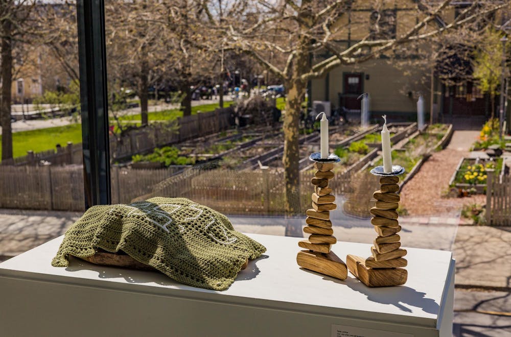 Photo of art pieces created by Talia LeVine ’27 displayed at the Brown Art Institute’s new “Point of Entry” exhibit. The piece on the left is a small green blanket covering a wooden bowl, and the piece on the right consists of two wooden towers with candles on top.