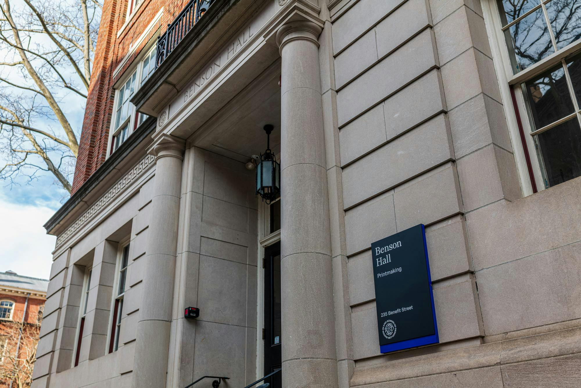 A photo of the Rhode Island School of Design's Benson Hall building with a sign containing the building name and description: "Benson Hall, Printmaking."