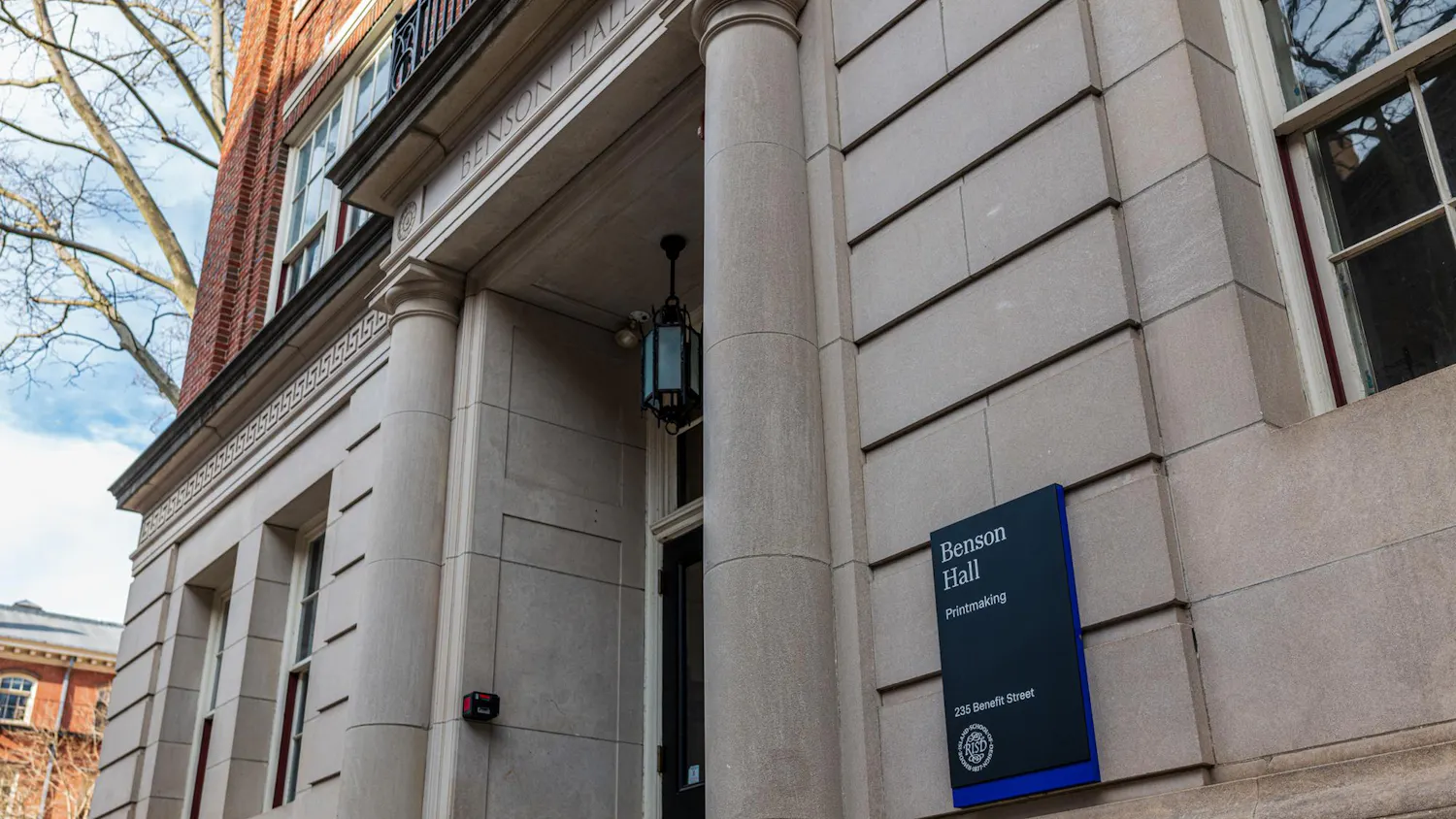 A photo of the Rhode Island School of Design's Benson Hall building with a sign containing the building name and description: "Benson Hall, Printmaking."