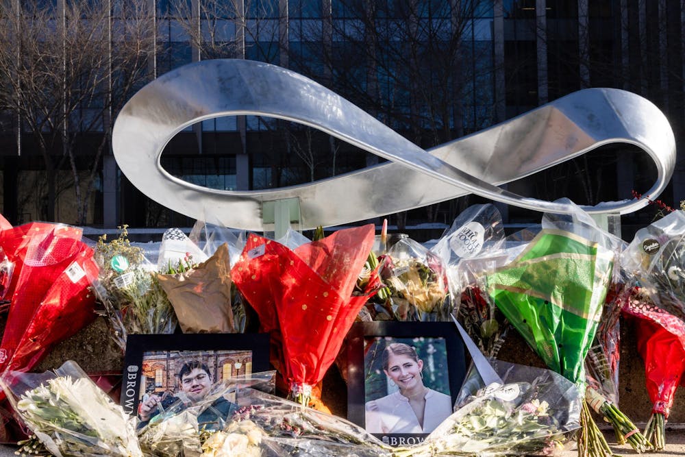 A memorial of flowers in front of Brown University's Barus & Holley Building. Centered within the flowers are framed portraits of Ella Cook and Mukhammad Aziz Umurzokov. 