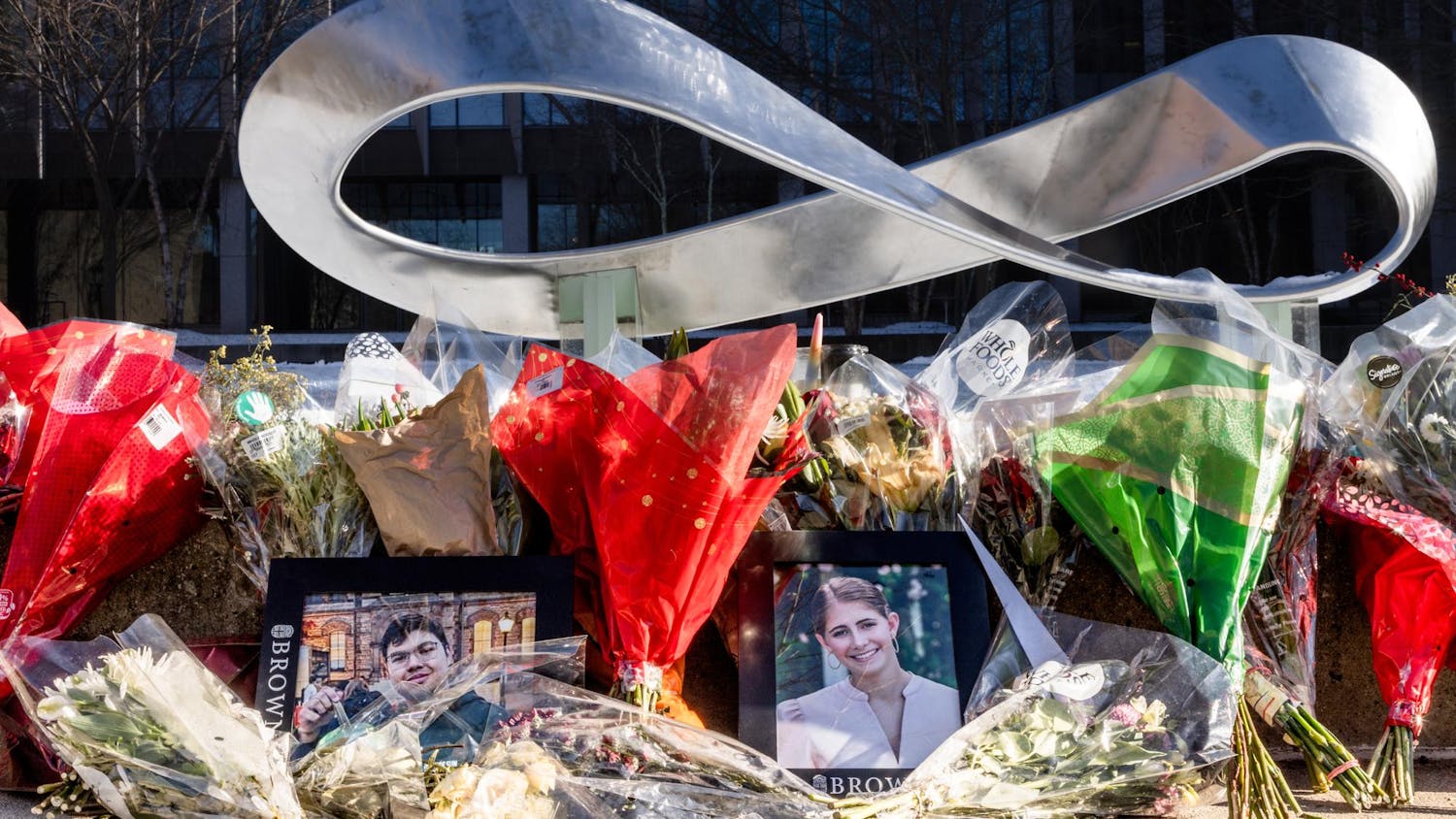 A memorial of flowers in front of Brown University's Barus & Holley Building. Centered within the flowers are framed portraits of Ella Cook and Mukhammad Aziz Umurzokov.
