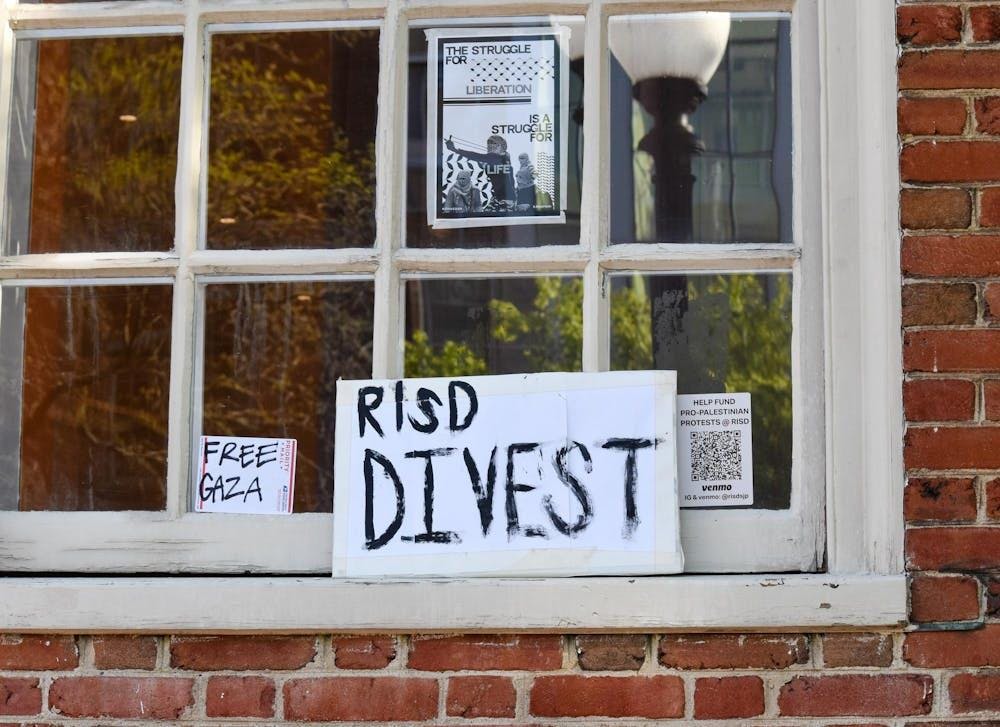 Photo of a posters in a window with black lettering that reads "RISD Divest" and "Free Gaza"