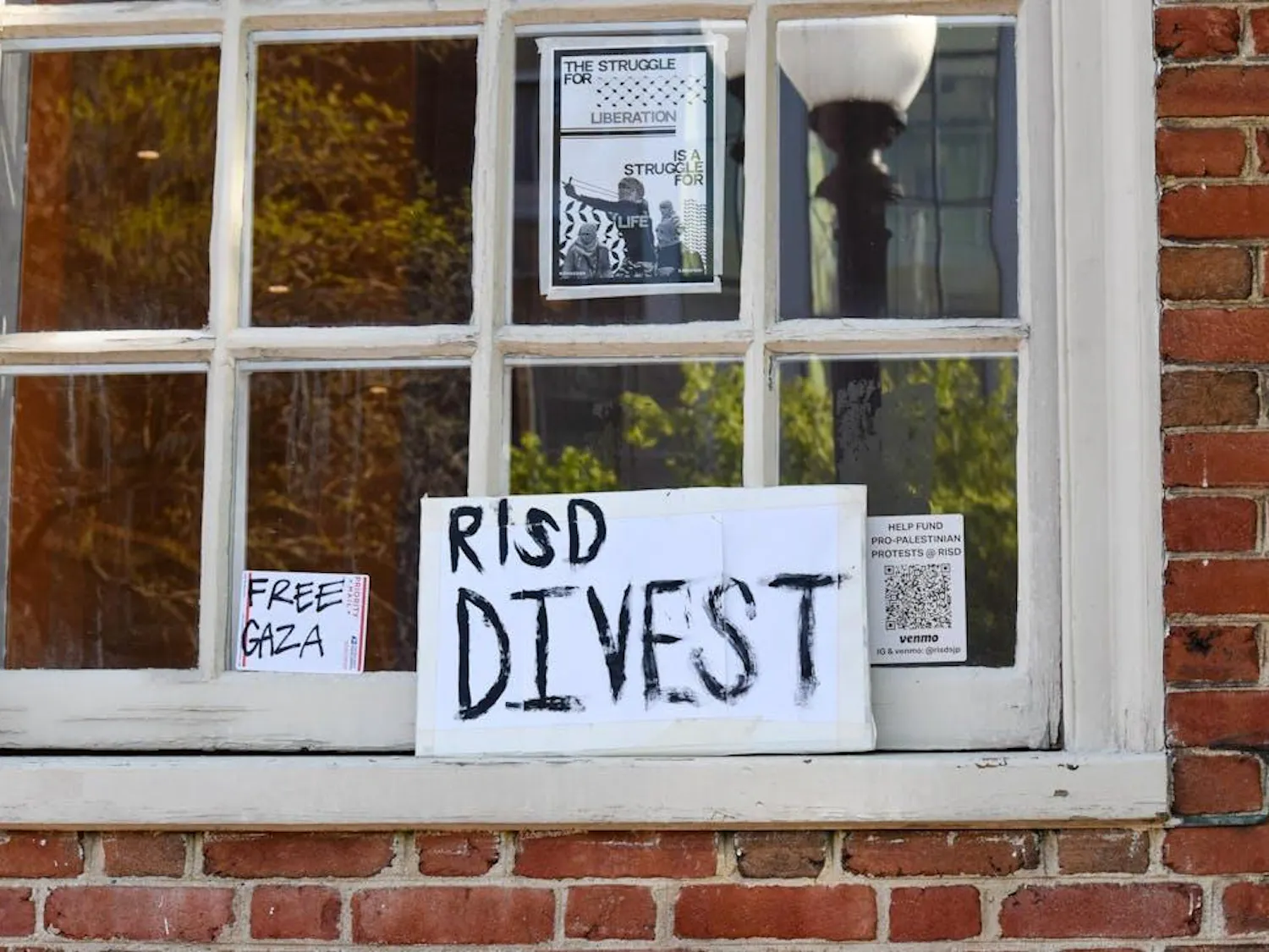 Photo of a posters in a window with black lettering that reads "RISD Divest" and "Free Gaza"