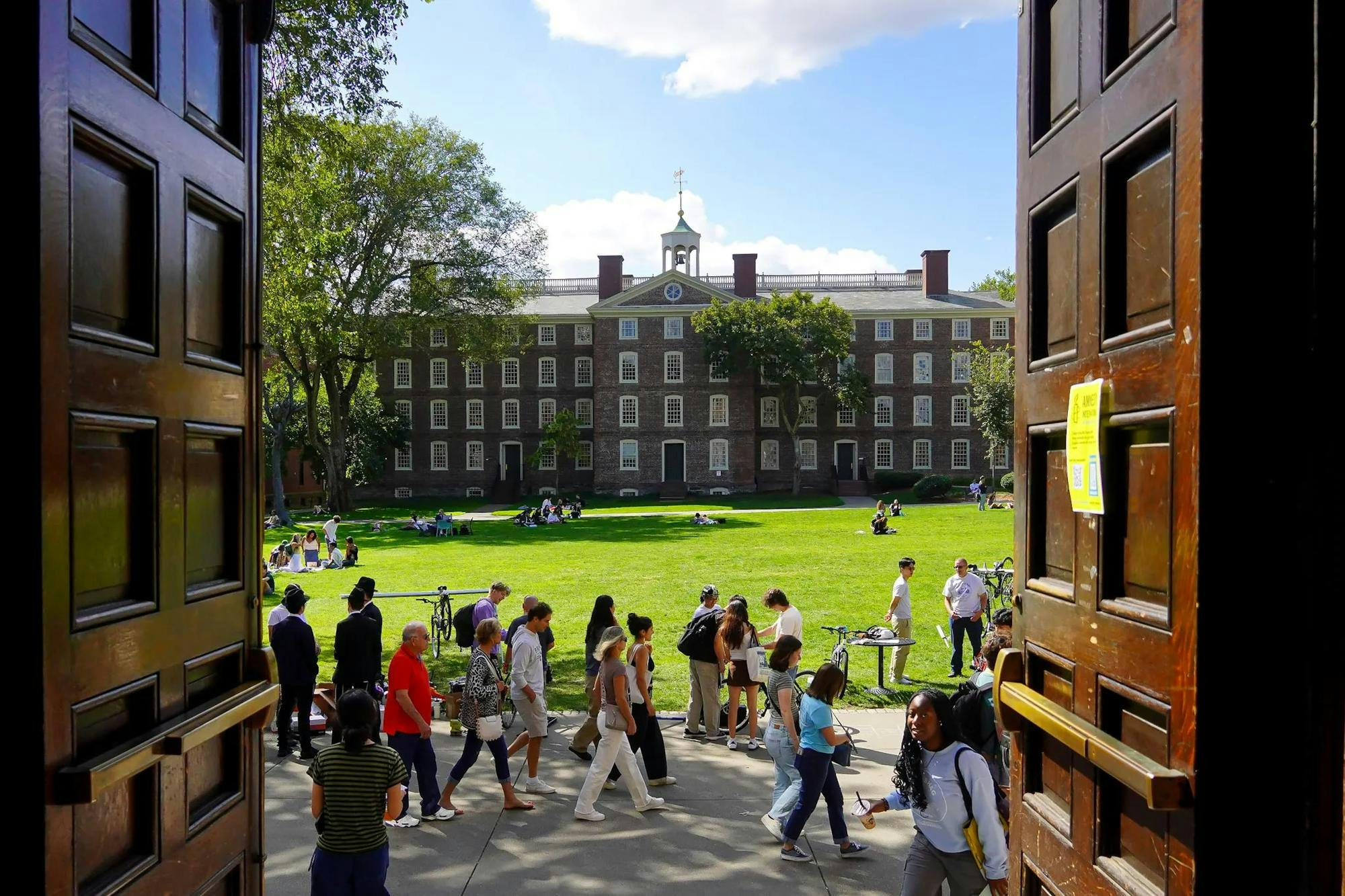 Photo of University Hall. The foreground features include Sayles Hall’s open doors and a group of students on the walkway.

