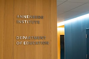 On a wood wall, metal letters spelling out "Annenberg Institute" on top and "Department of Education" on the bottom. There is dark blue wall to the right. 