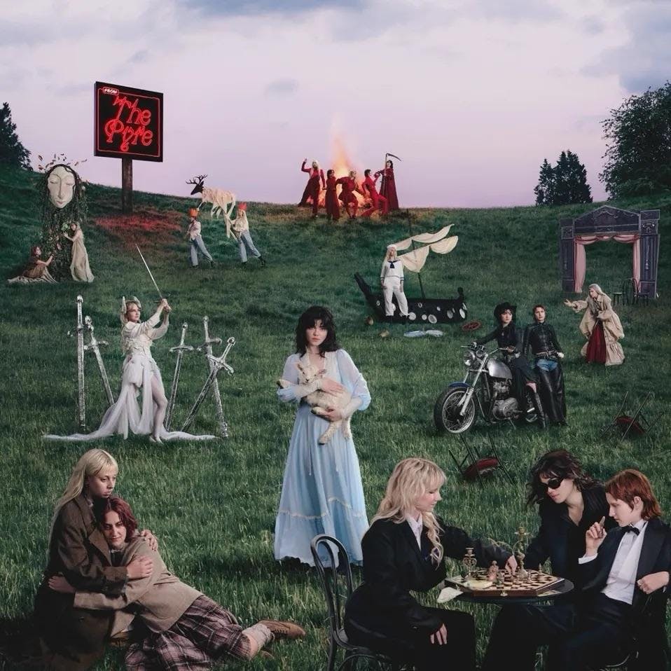 Album cover for ‘From the Pyre’ by The Last Dinner Party, which shows a series of figrures and scenes placed disparately around a grassy hill. The central figure, a woman in a blue dress, holds a lamb. At the top of the hill, several figures dressed in red move around a burning pyre.