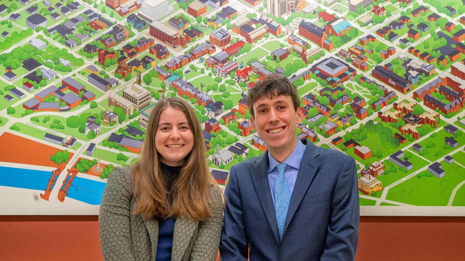 A photo of admissions officers Emily Wagg ’24 and Aidan Berman ’25 in front of a cartoon map of Brown University.