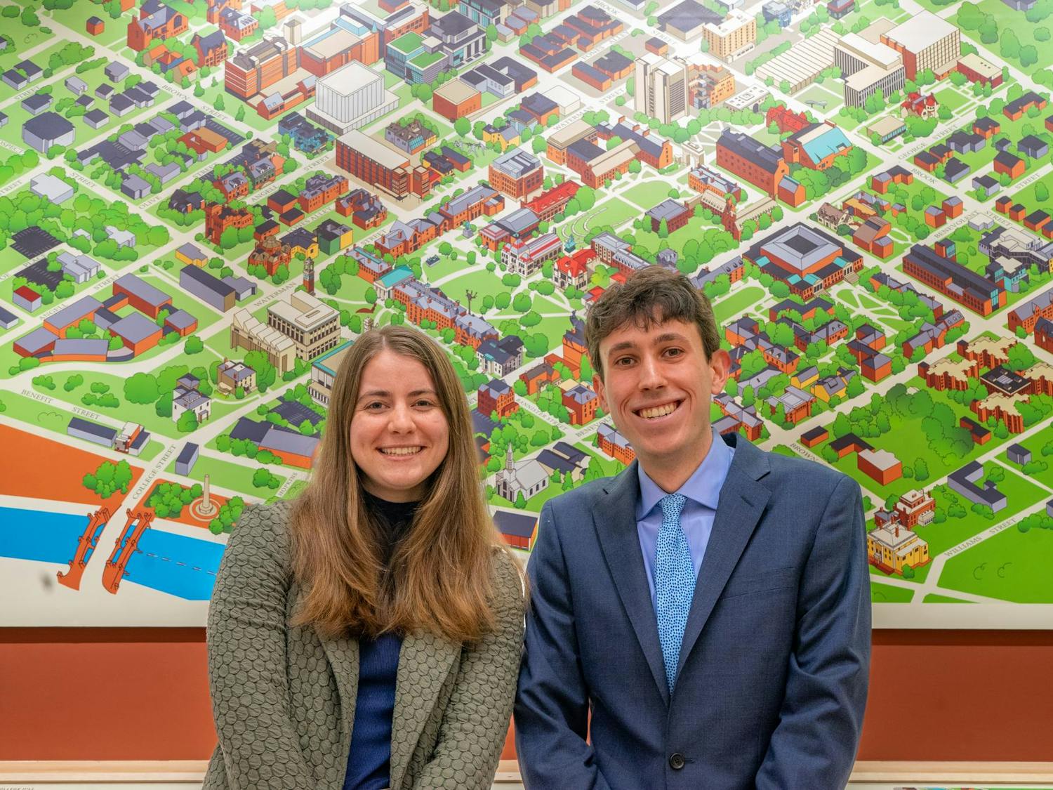 A photo of admissions officers Emily Wagg ’24 and Aidan Berman ’25 in front of a cartoon map of Brown University.