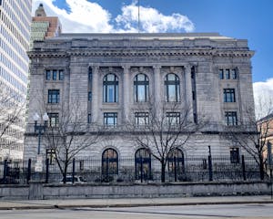 A large pale gray stone building with large windows and columns.