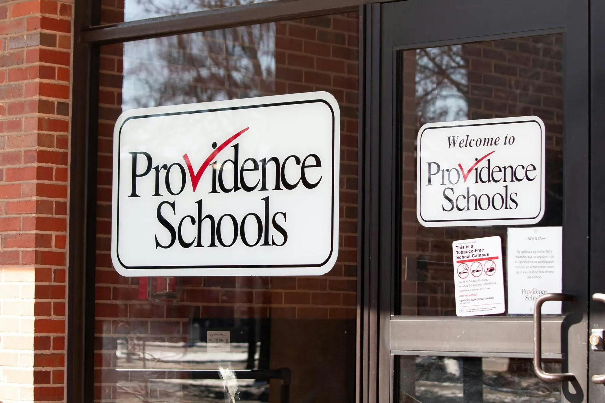 Photo of the entrance of the Providence Schools Department, with a white “Providence Schools” sign on the glass.