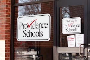 Photo of the entrance of the Providence Schools Department, with a white “Providence Schools” sign on the glass.