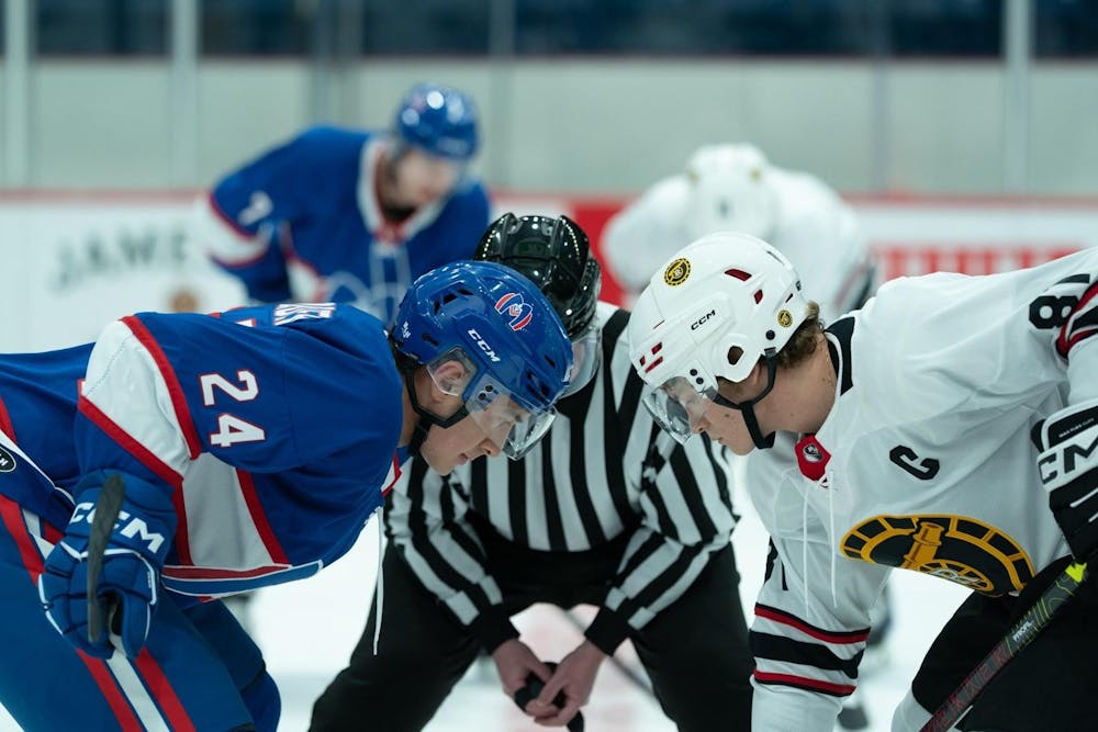 Two male hockey players tensely face each other on the ice, one in a blue uniform and the other in white. 