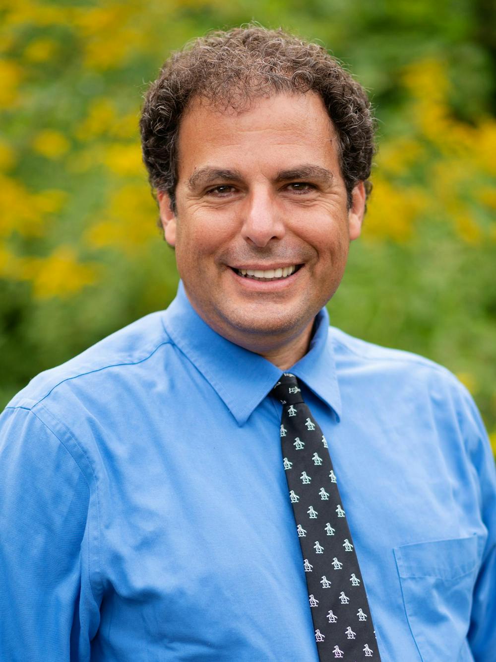 A headshot of Michael Littman in front of a green backdrop in a blue shirt.