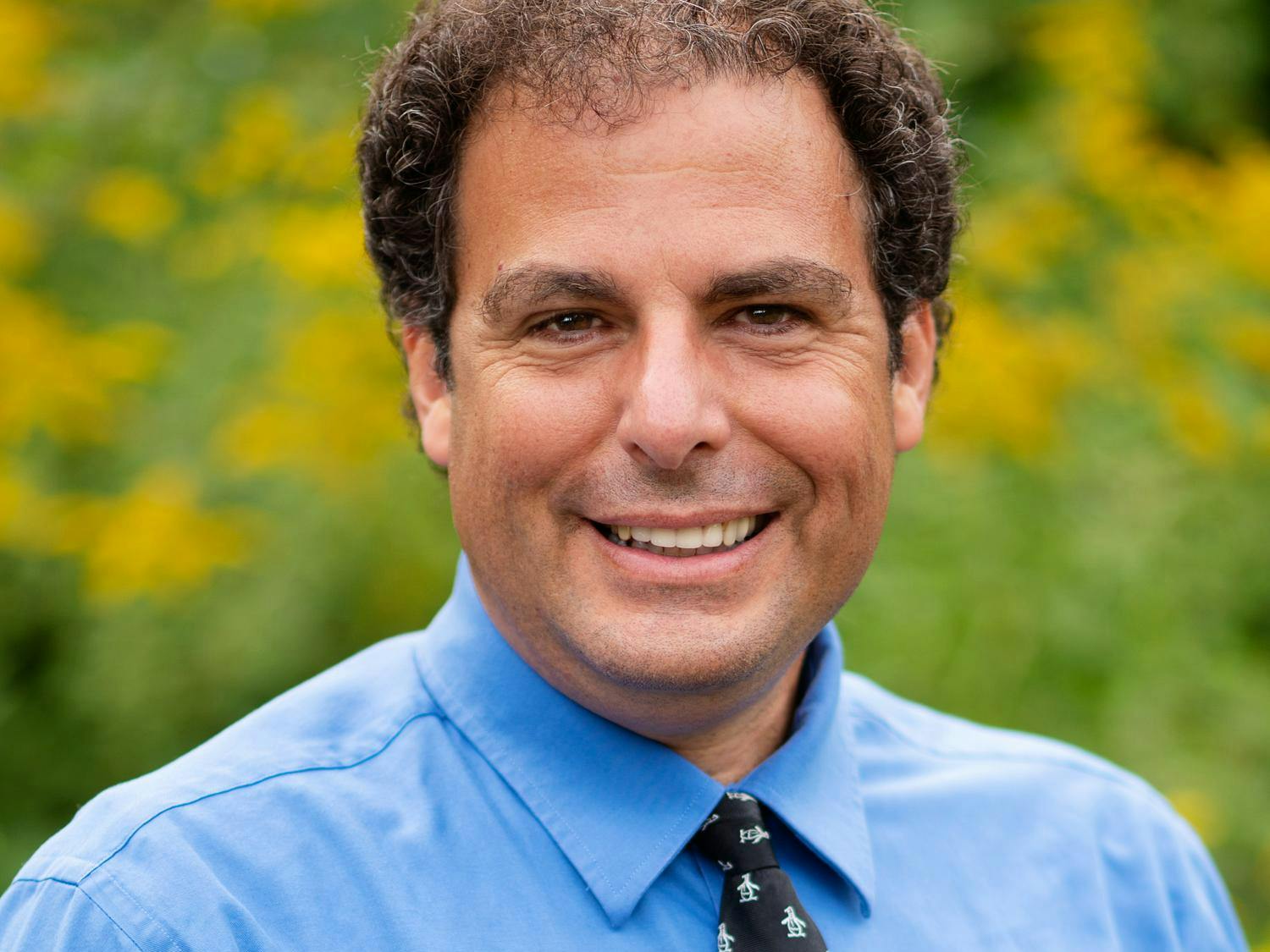 A headshot of Michael Littman in front of a green backdrop in a blue shirt.
