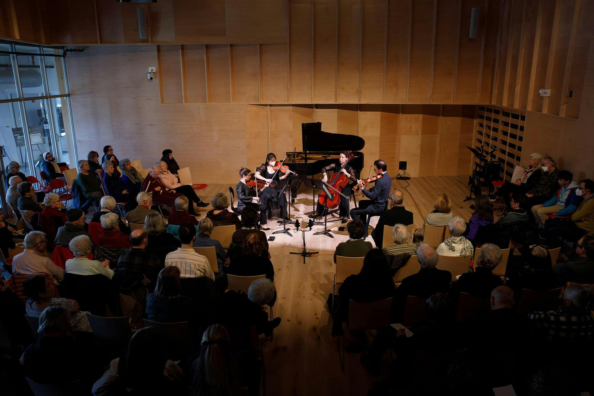 An audience sits in a performance hall and listens to a performance by a string quartet. 