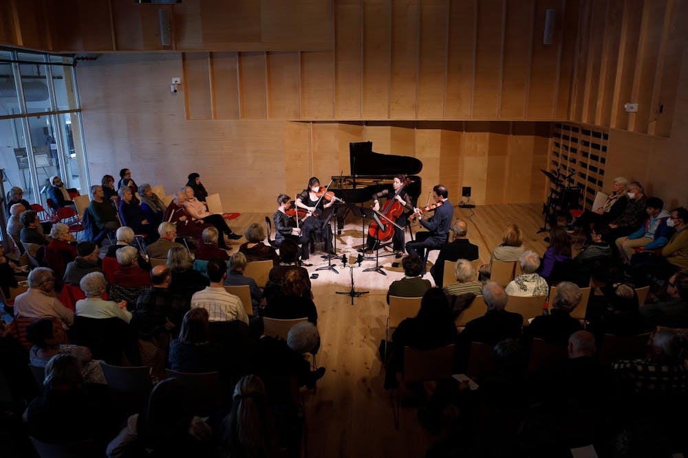 An audience sits in a performance hall and listens to a performance by a string quartet. 