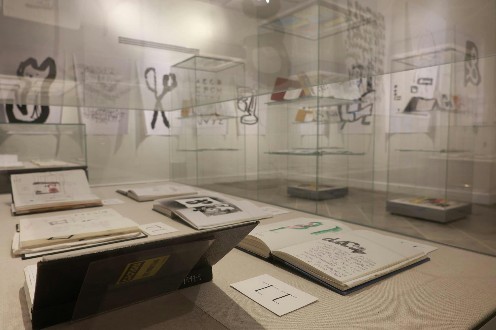 Photo of the “Everywhere I Go,” exhibit at the Providence Public Library on Tuesday, featuring sketchbooks open and on display in clear display cases with various larger drawings displayed on the walls.