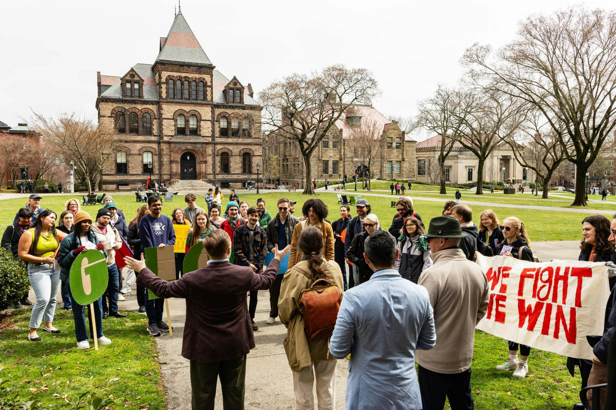 A man stands on the Main Green holding his hands out, addressing rally attendees.