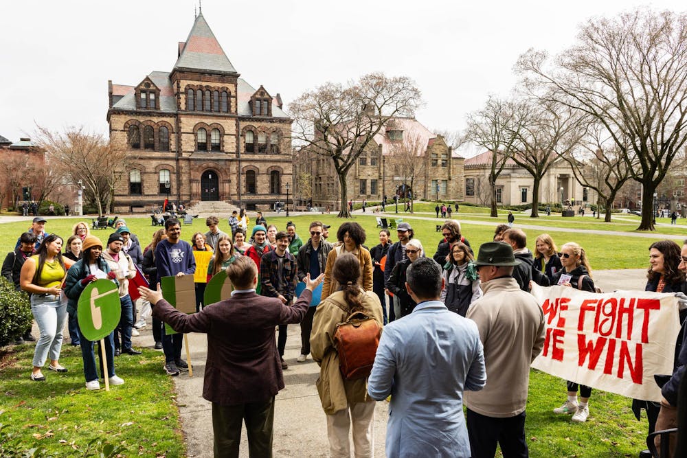 A man stands on the Main Green holding his hands out, addressing rally attendees.