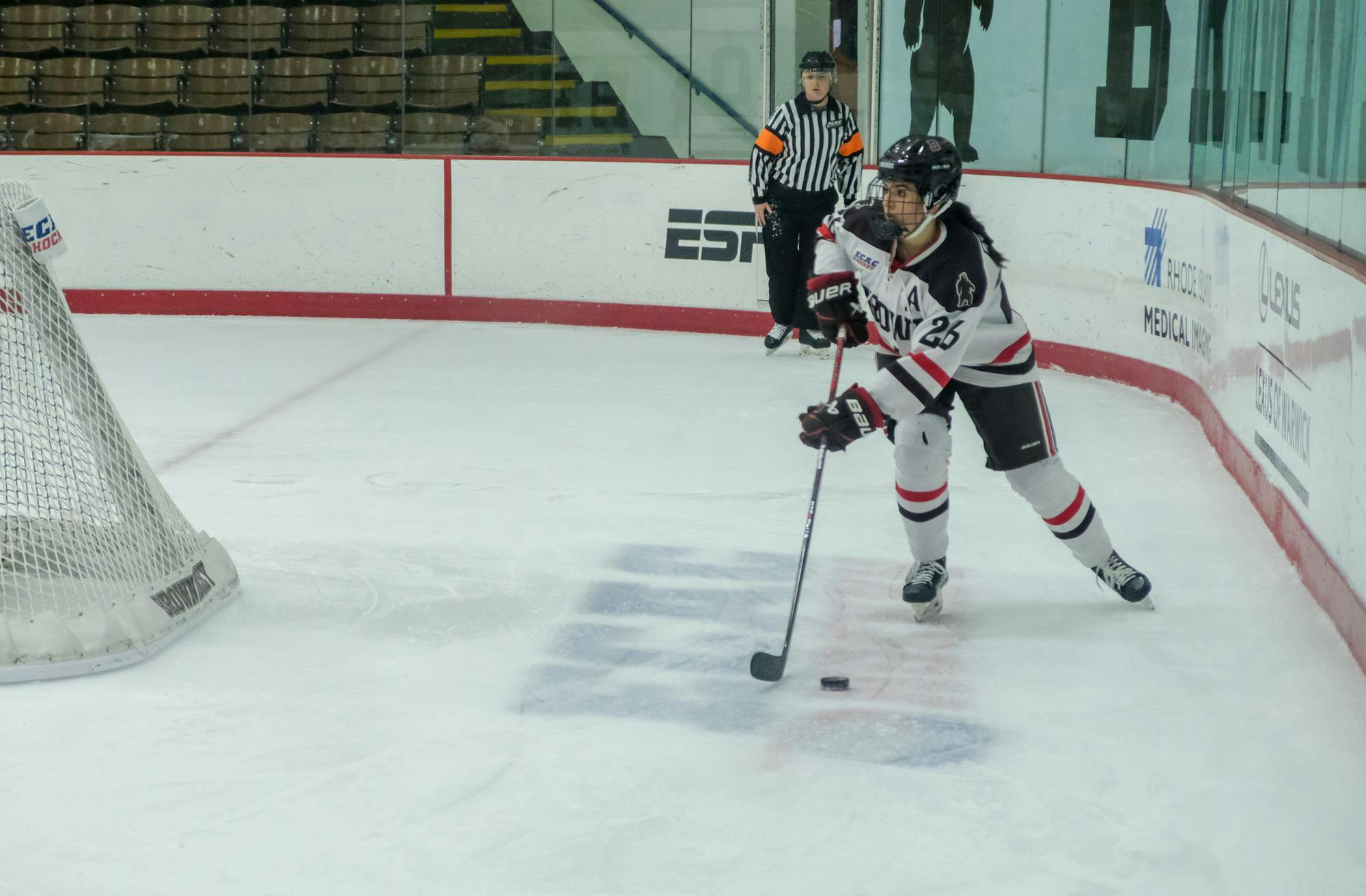 India McDadi skates behind the goal with the puck at her ice hockey stick as a referee trails behind her.