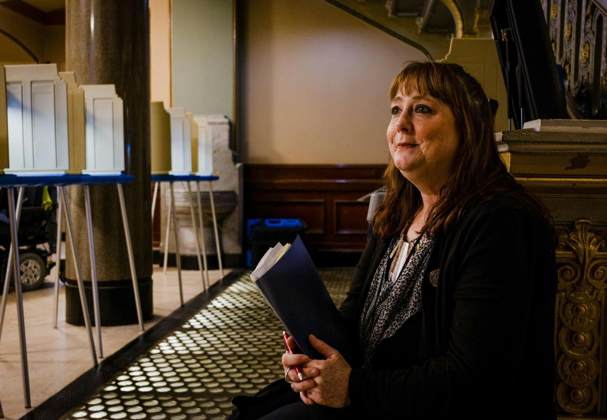 A poll worker, holding a folder, looks front.