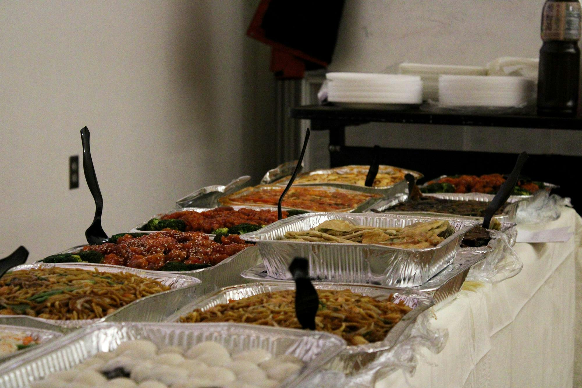 Photo of assorted traditional Chinese food in aluminum pans with big plastic spoons sticking out of some.

