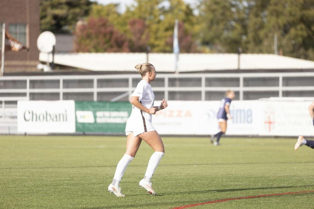 A photo of a Brown women’s soccer player running on the turf.