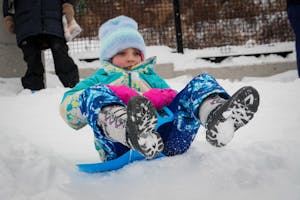 A young girl in colorful snow gear sleds down a snowy hill.