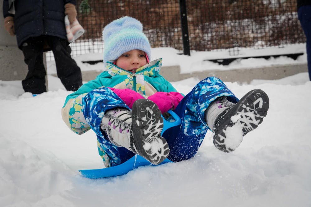 A young girl in colorful snow gear sleds down a snowy hill.