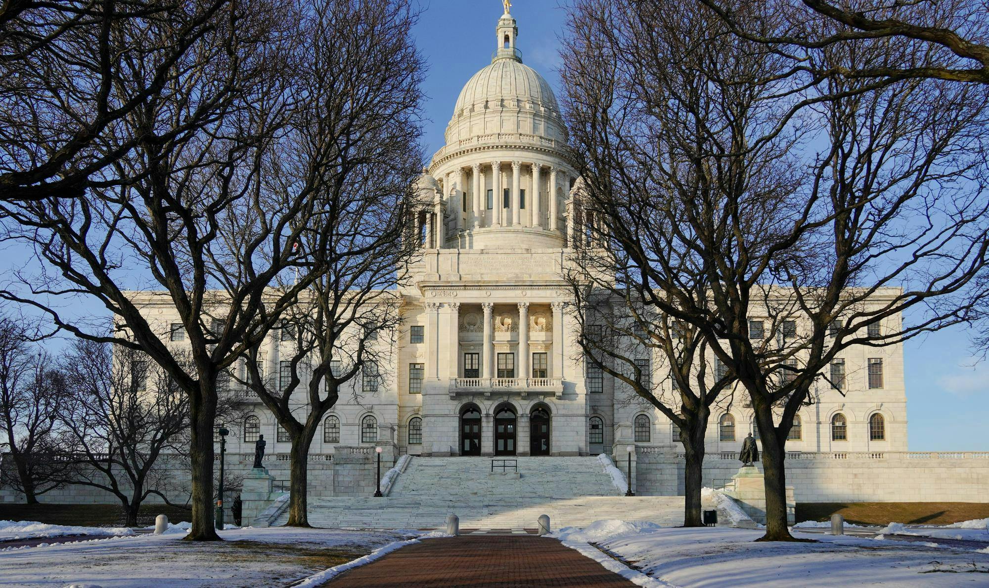 A photo of the Rhode Island State House in winter with two trees in front of the building. 