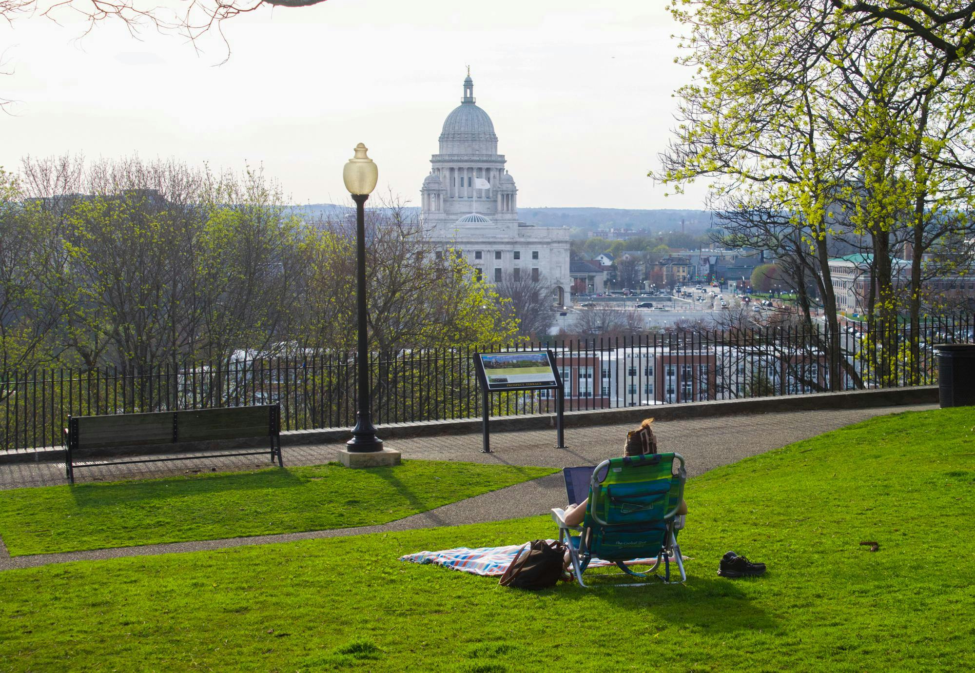 A photo of a person sitting in a camping chair on Prospect Terrace park looking over the balcony towards Rhode Island State House. 