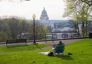 A photo of a person sitting in a camping chair on Prospect Terrace park looking over the balcony towards Rhode Island State House. 