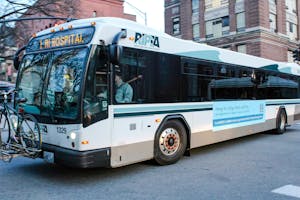 A Rhode Island Public Transit Authority bus, white with light and dark blue outlines with 1 RI Hospital being displayed in yellow text in the front in addition to a bicycle attached to the front.