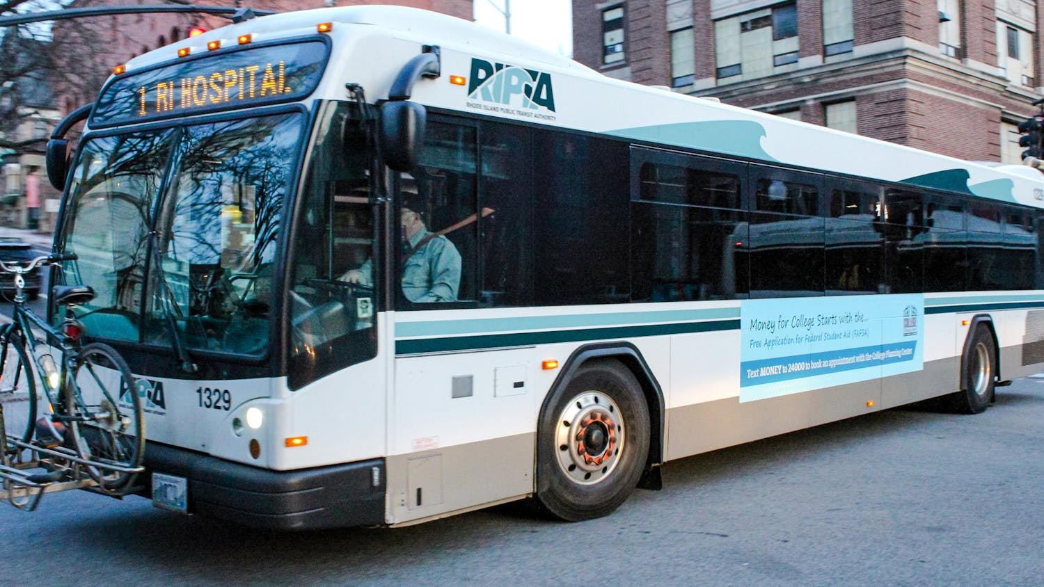 A Rhode Island Public Transit Authority bus, white with light and dark blue outlines with 1 RI Hospital being displayed in yellow text in the front in addition to a bicycle attached to the front.