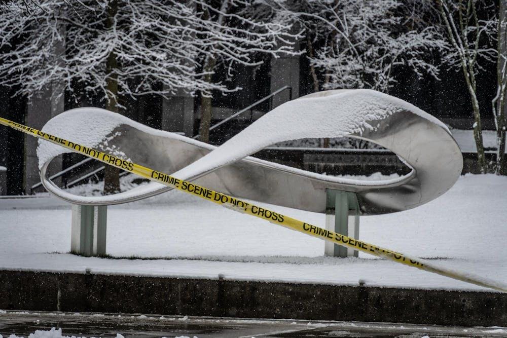 A silver infinity statue in front of Barus and Holley in the snow. Yellow crime scene tape crosses over the photo. 