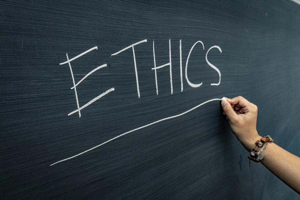A photo of a hand drawing a line with chalk under the word “ETHICS” written on a dark green chalkboard. 